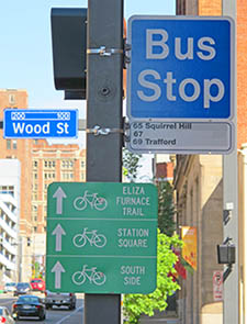 Signs for a Port Authority bus stop and for nearby bike trails, along with the street sign for Wood Street.