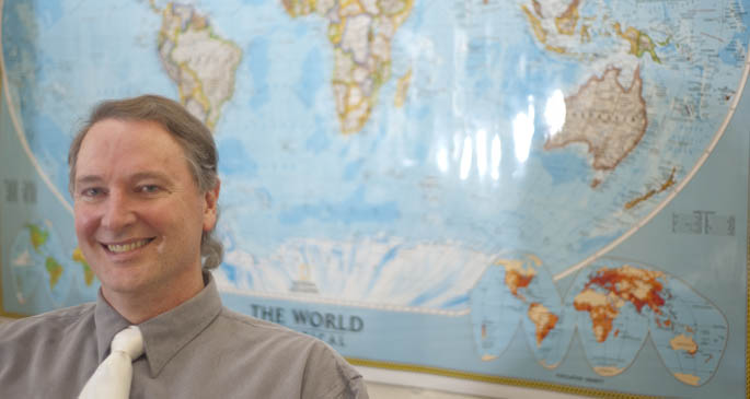 Assistant Professor Mike Finnegan sits in front of a map of the world