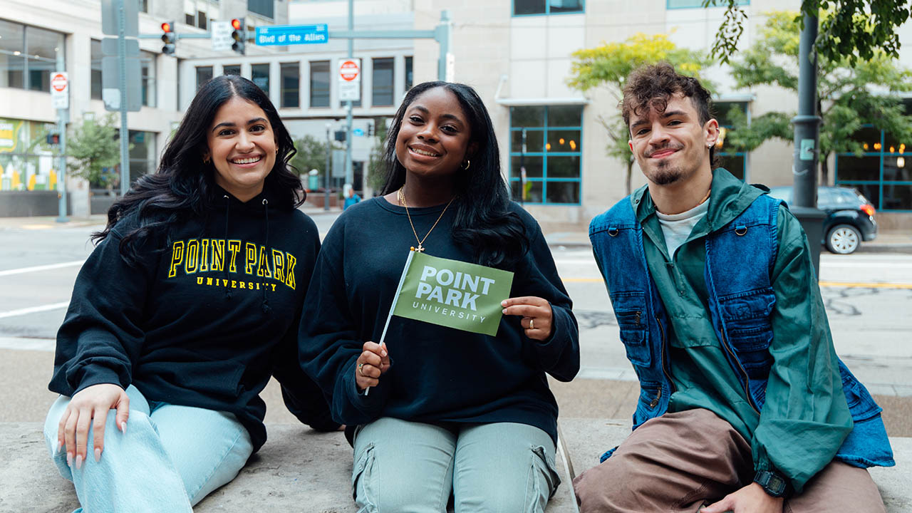 Point Park students hold a mini Point Park University flag in Village Park. 