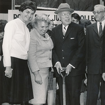 Four people stand around a shovel at a building groundbreaking.