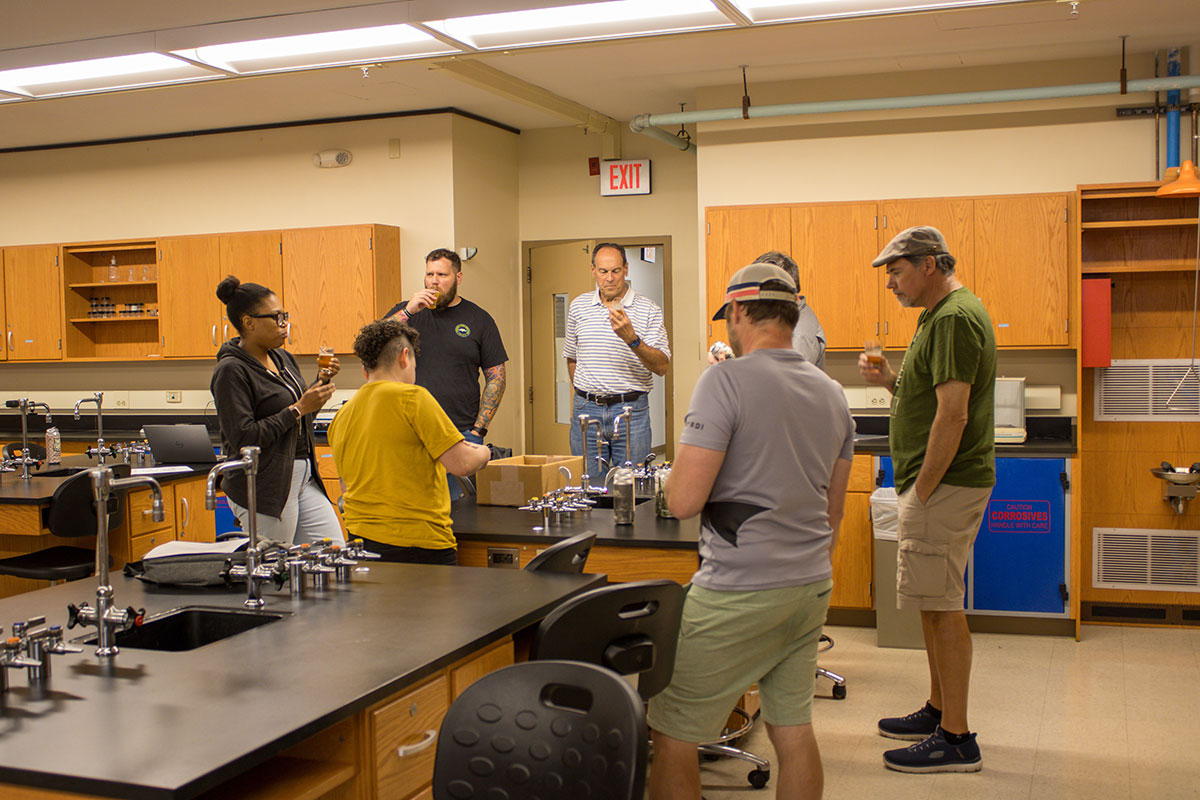 Adults stand around a lab tasting a drink