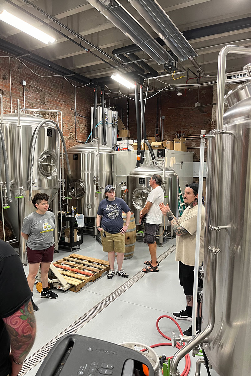 A group of people stand in a brewing room.