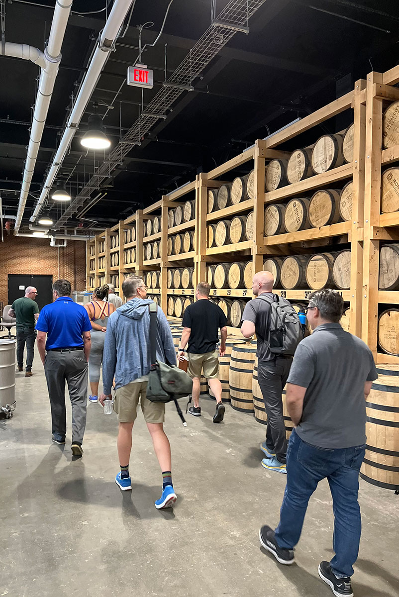 People walk in a room of whiskey barrels.