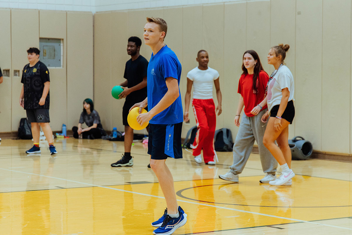 Students play dodgeball in a gym.