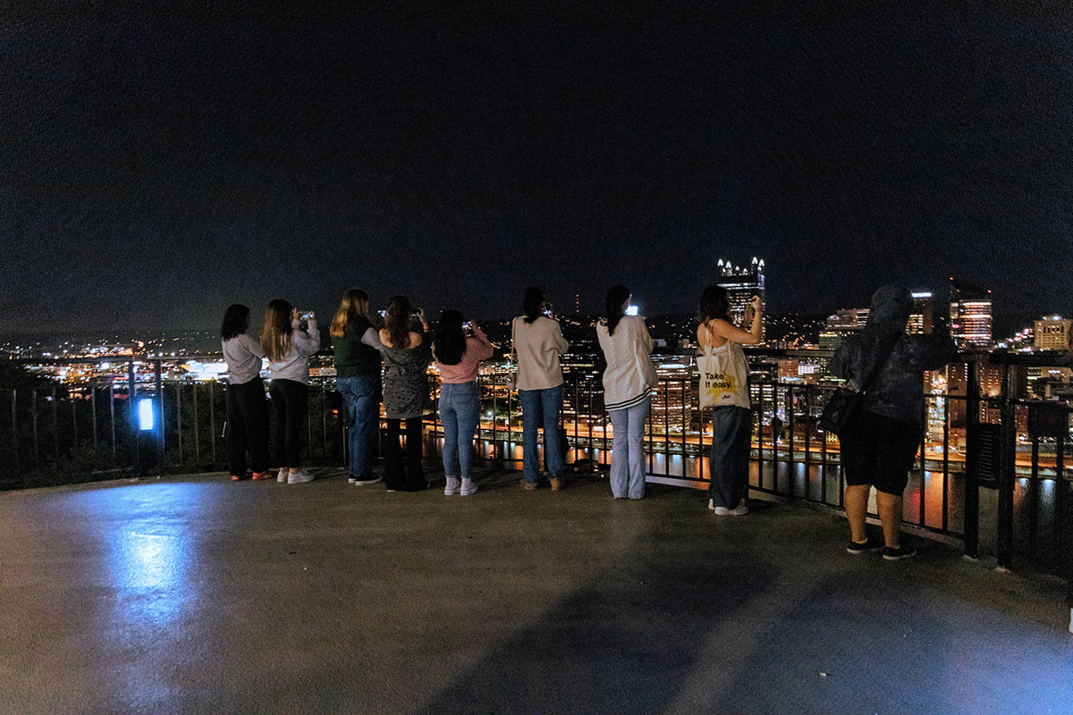 Students stand on Mt. Washington with the city behind him in the night.