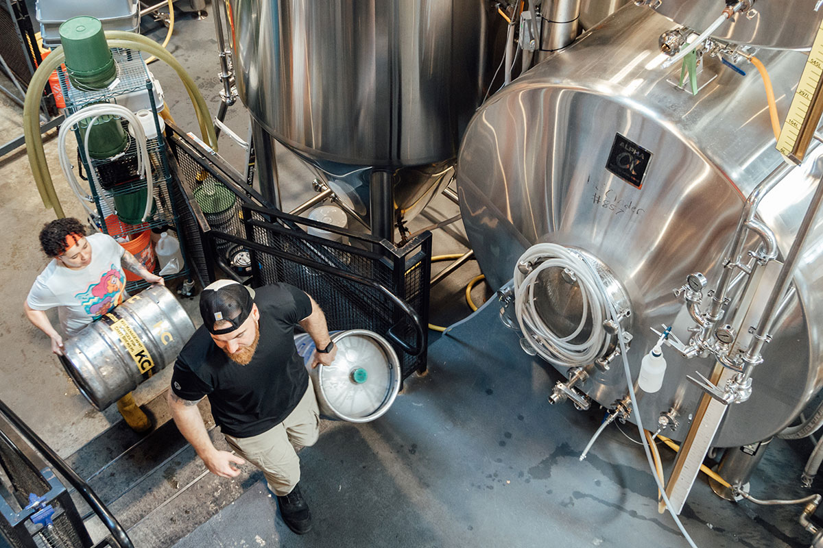 Two people carry kegs through a brewery.