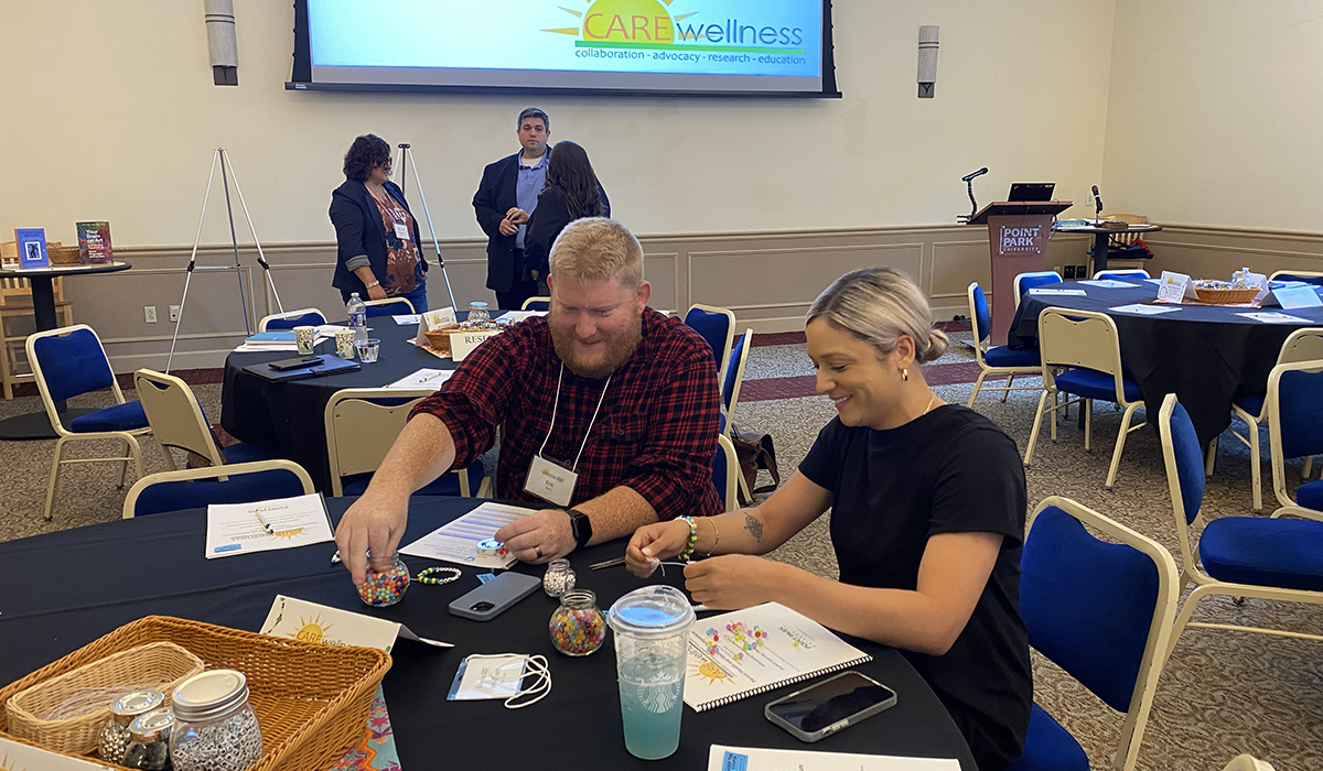 Pictured are two symposium attendees smiling and making friendship bracelets. Photo by Nicole Chynoweth.