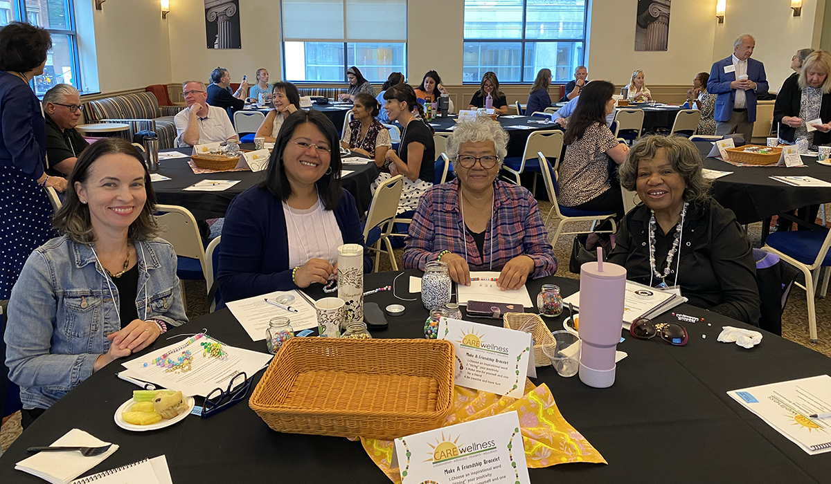 Pictured are four symposium attendees smiling and making friendship bracelets. Photo by Nicole Chynoweth.