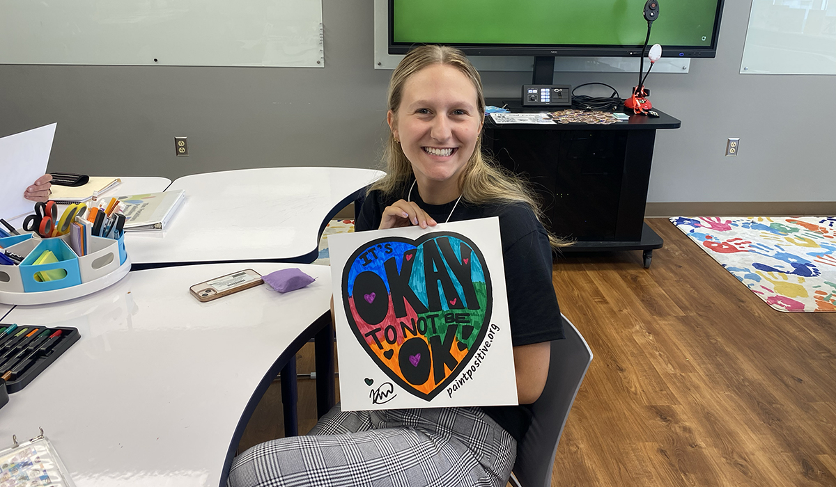 Lily Marchand poses for a photo with the poster she colored during the workshop session with The Positive Painting Project. Photo by Nicole Chynoweth.