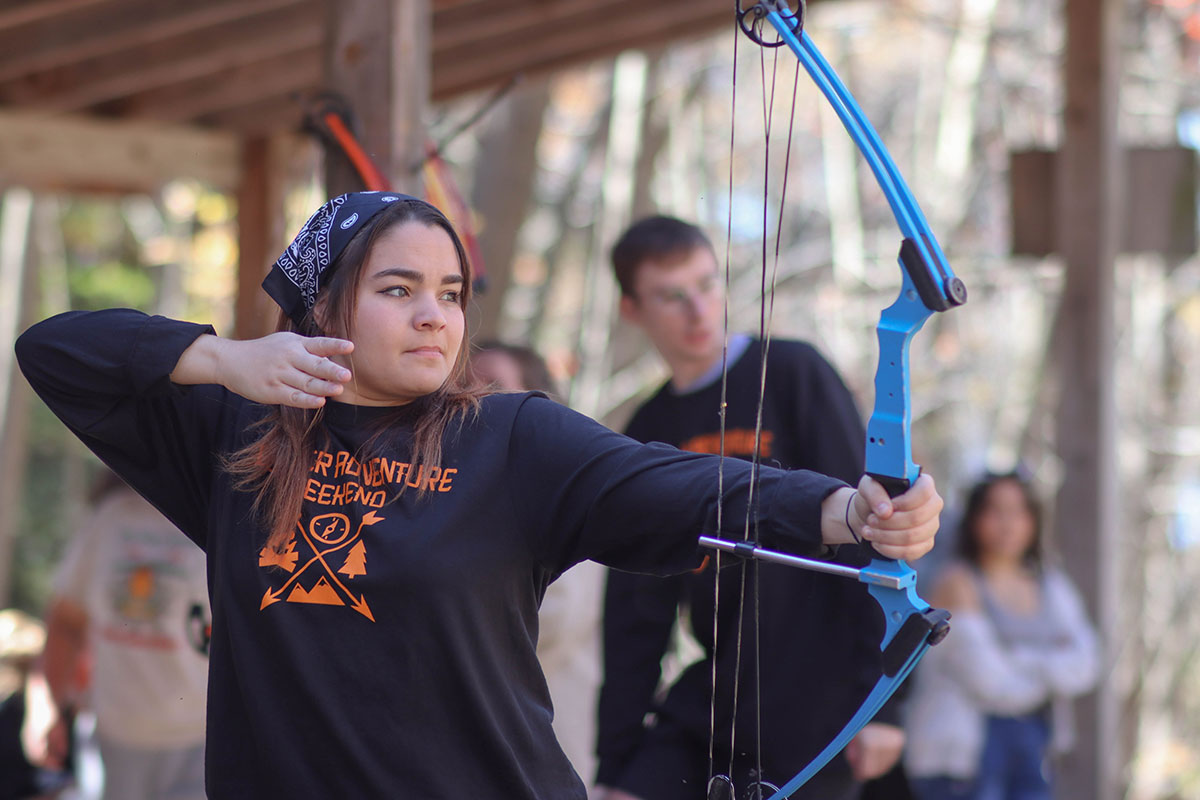 A student pulls back an archery bow.