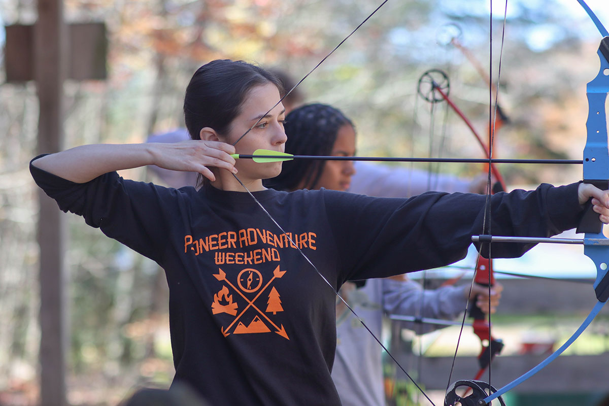 A student pulls back an archery bow.