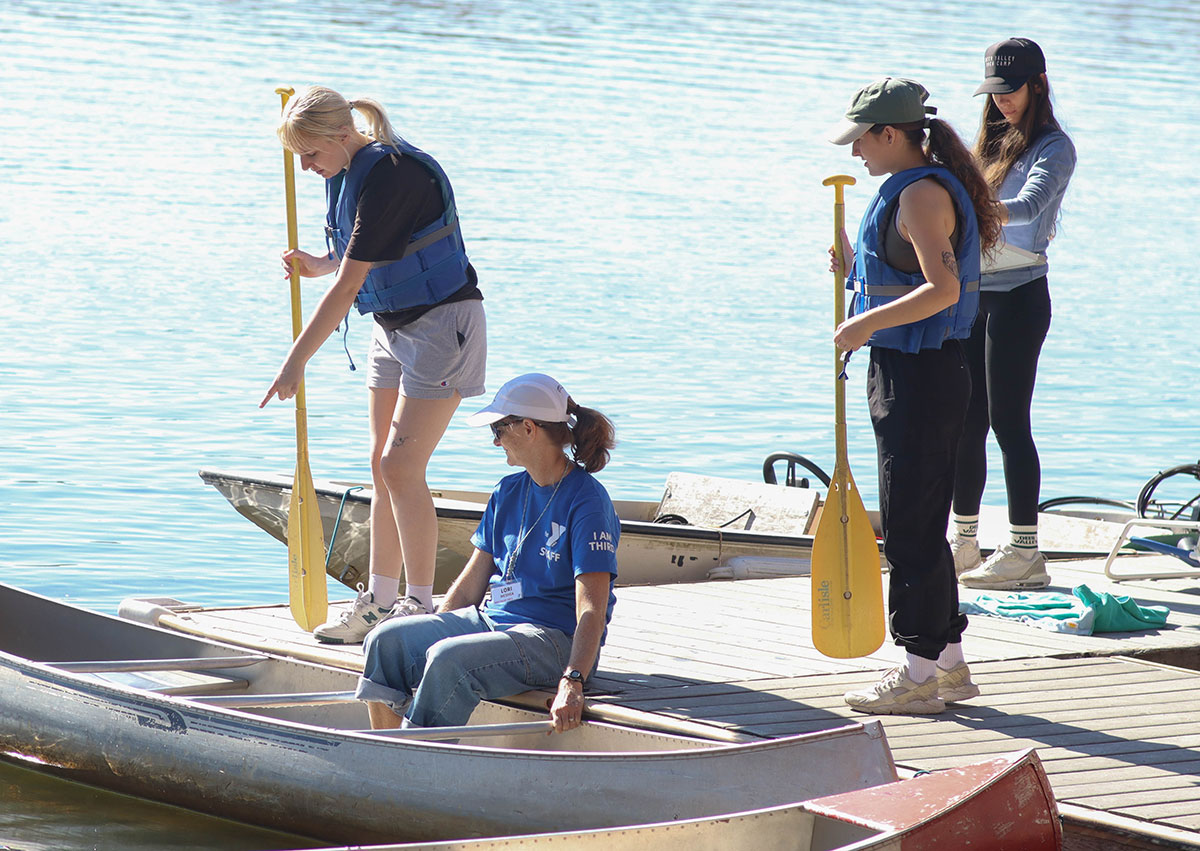 Students wearing life jackets stand around a boat.