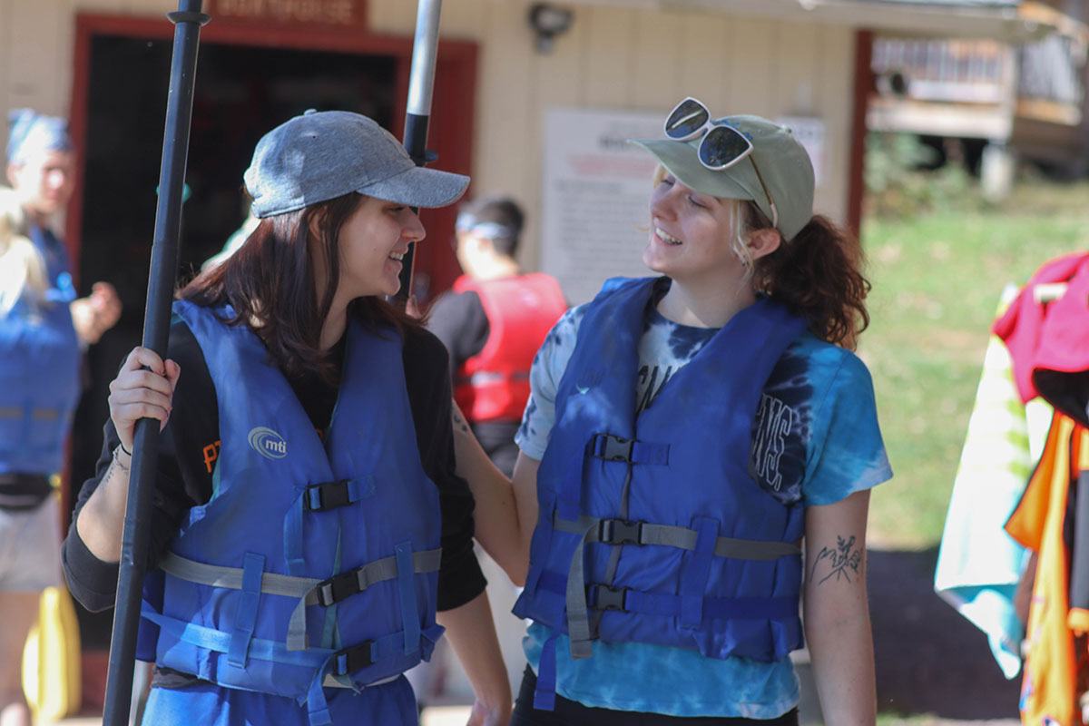 Two students wearing life jackets smile at one another.