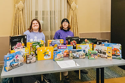 Two students sit behind a table of Lego boxes.