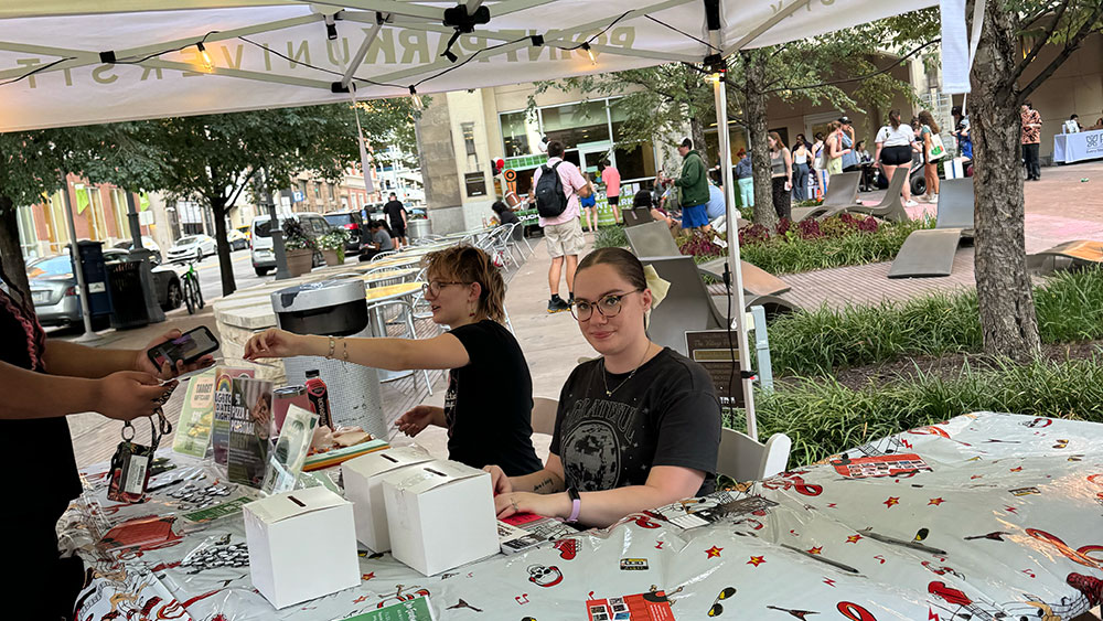 Two students sit at a table under a tent.