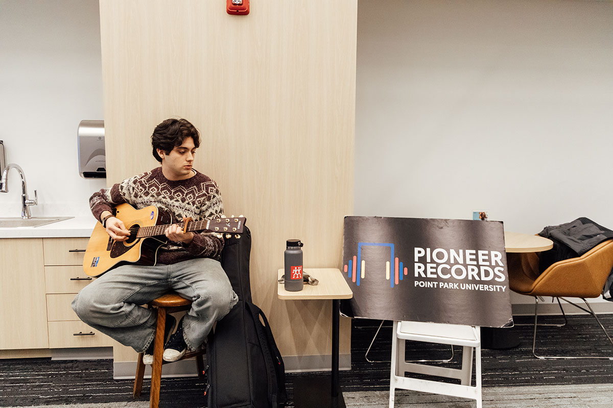 A student plays the guitar near a Pioneer Records sign.