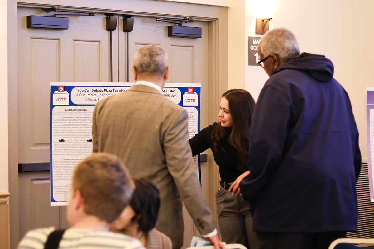 A girl stands beside a poster and has a conversation with other people