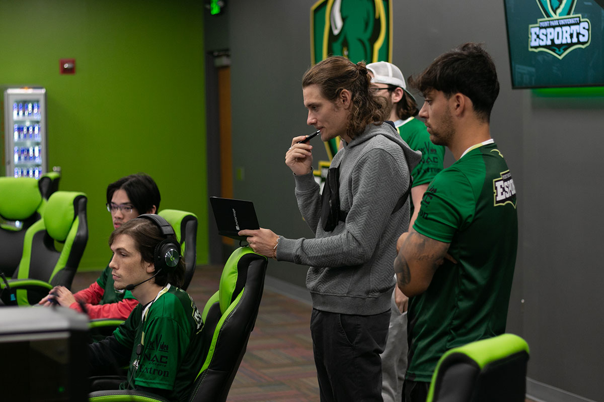 A man stands behind a student playing on the computer.