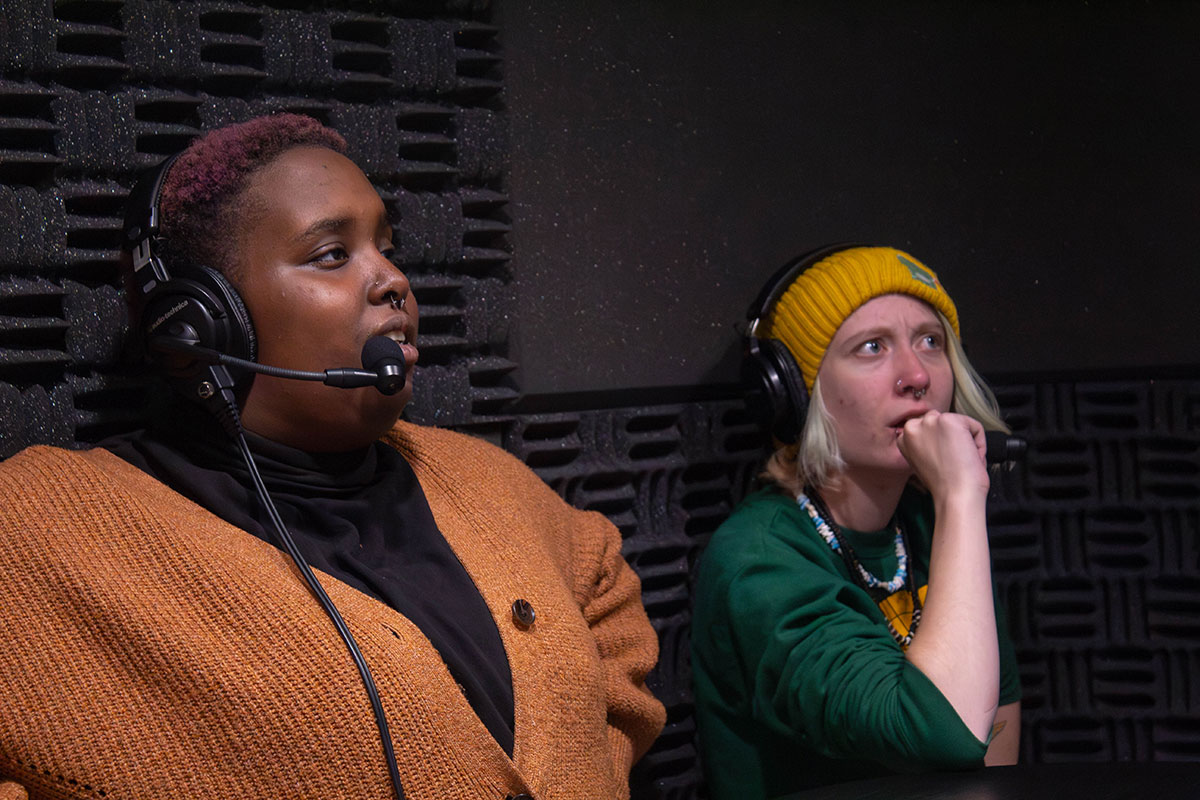 Two students wearing headsets announce a video game.