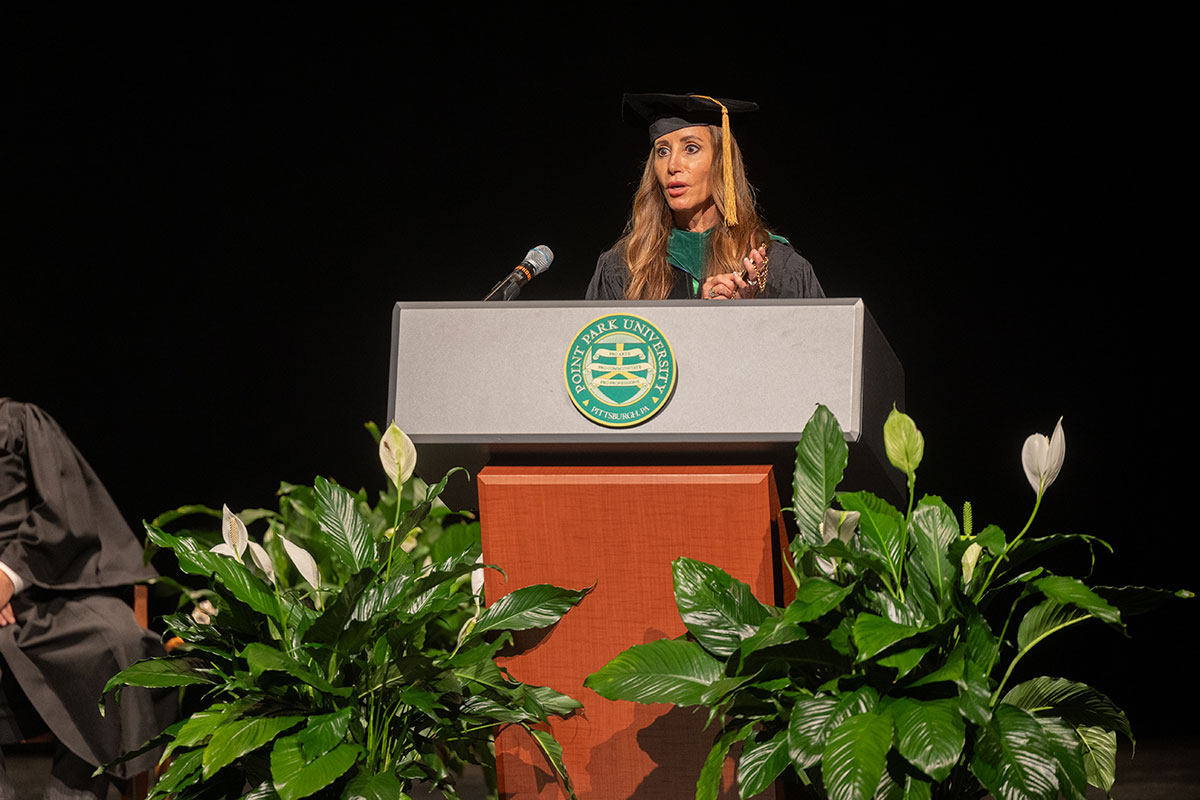 A woman in regalia speaks at a podium.