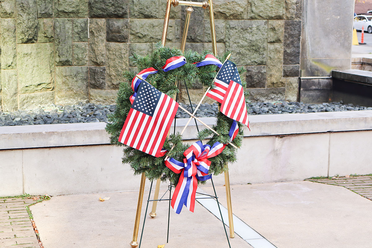 A wreath with American flags sits in front of the Village Park fountain.