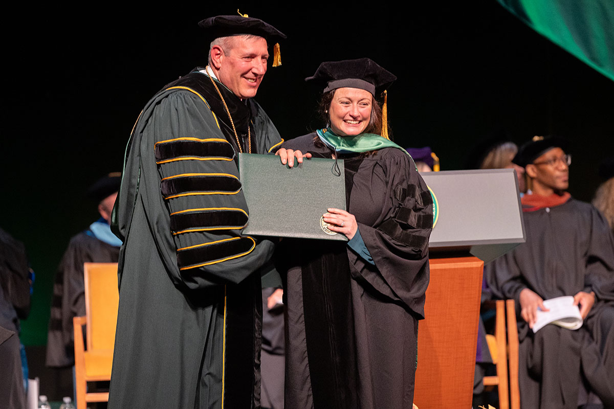 Chris Brussalis hands a diploma to a graduate.