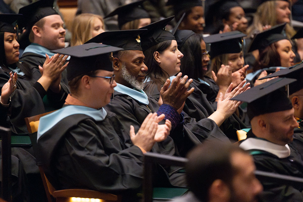 Graduates sit in seats clapping. 