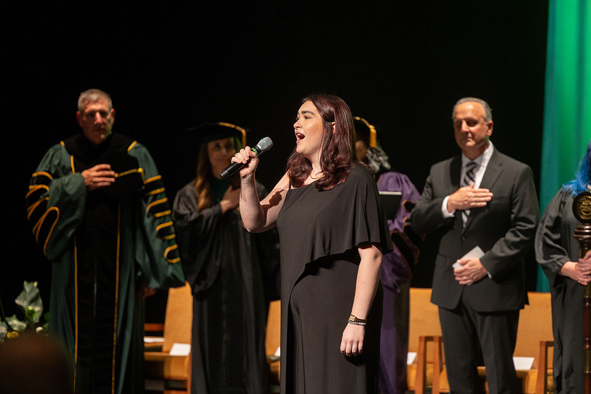 A woman sings on a stage with people behind her. 