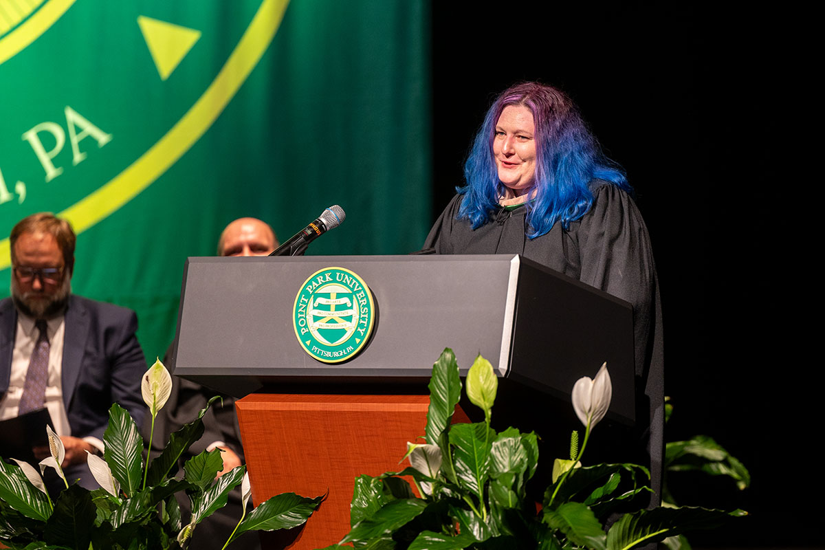 A woman in regalia stands at a podium.