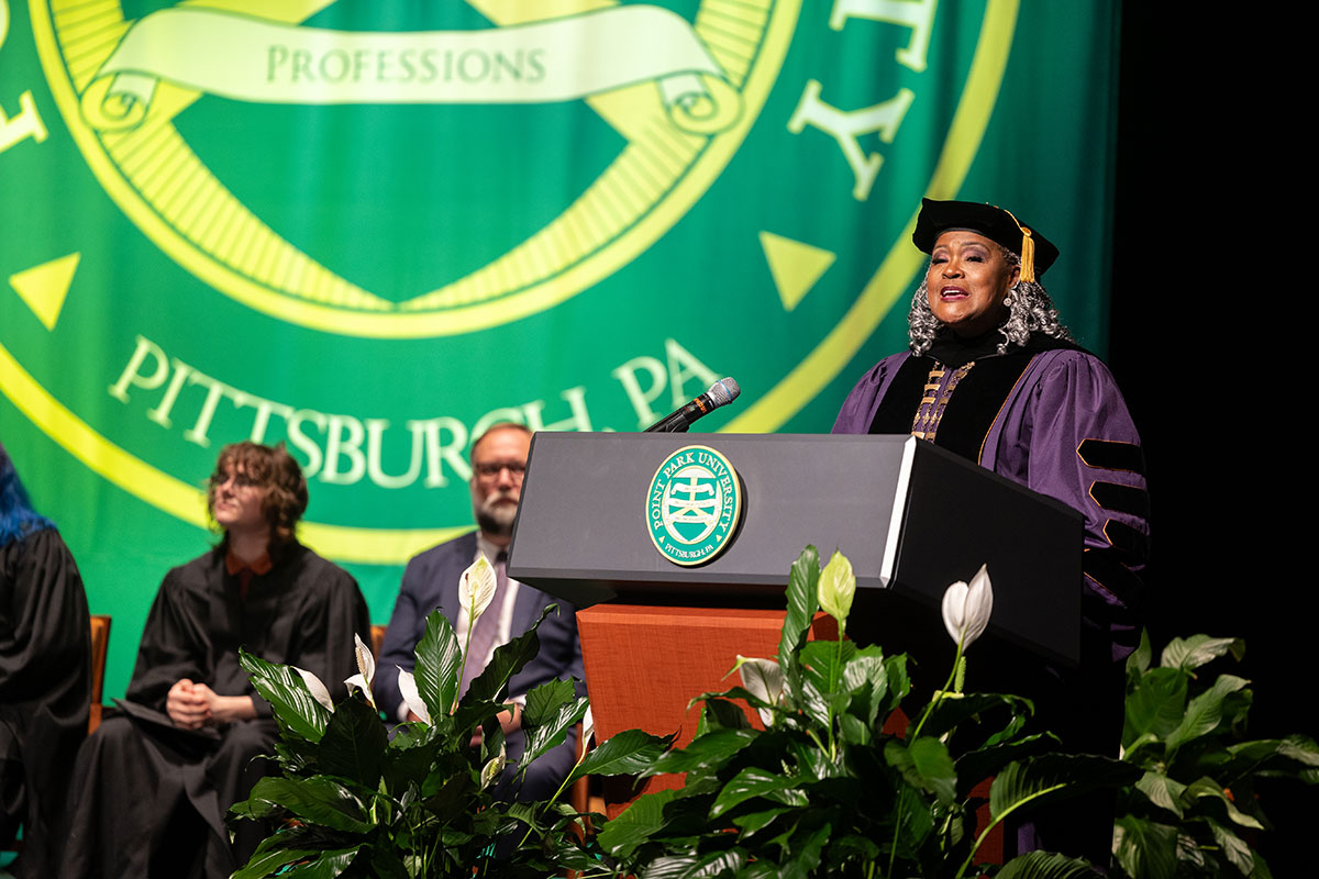 A woman in regalia speaks from a podium. 