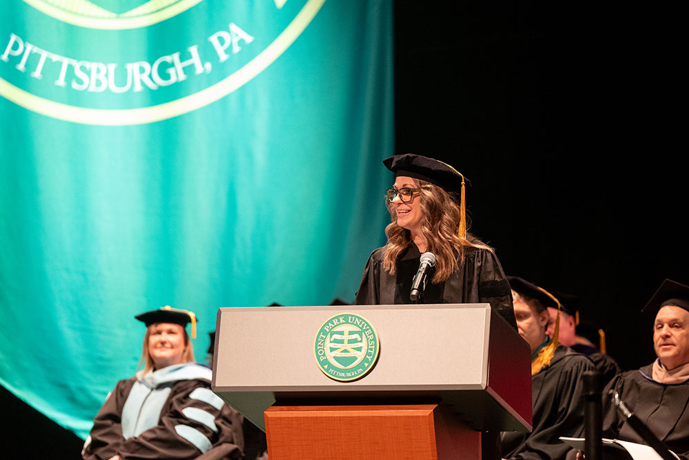 A woman in academic regalia speaks at a podium.