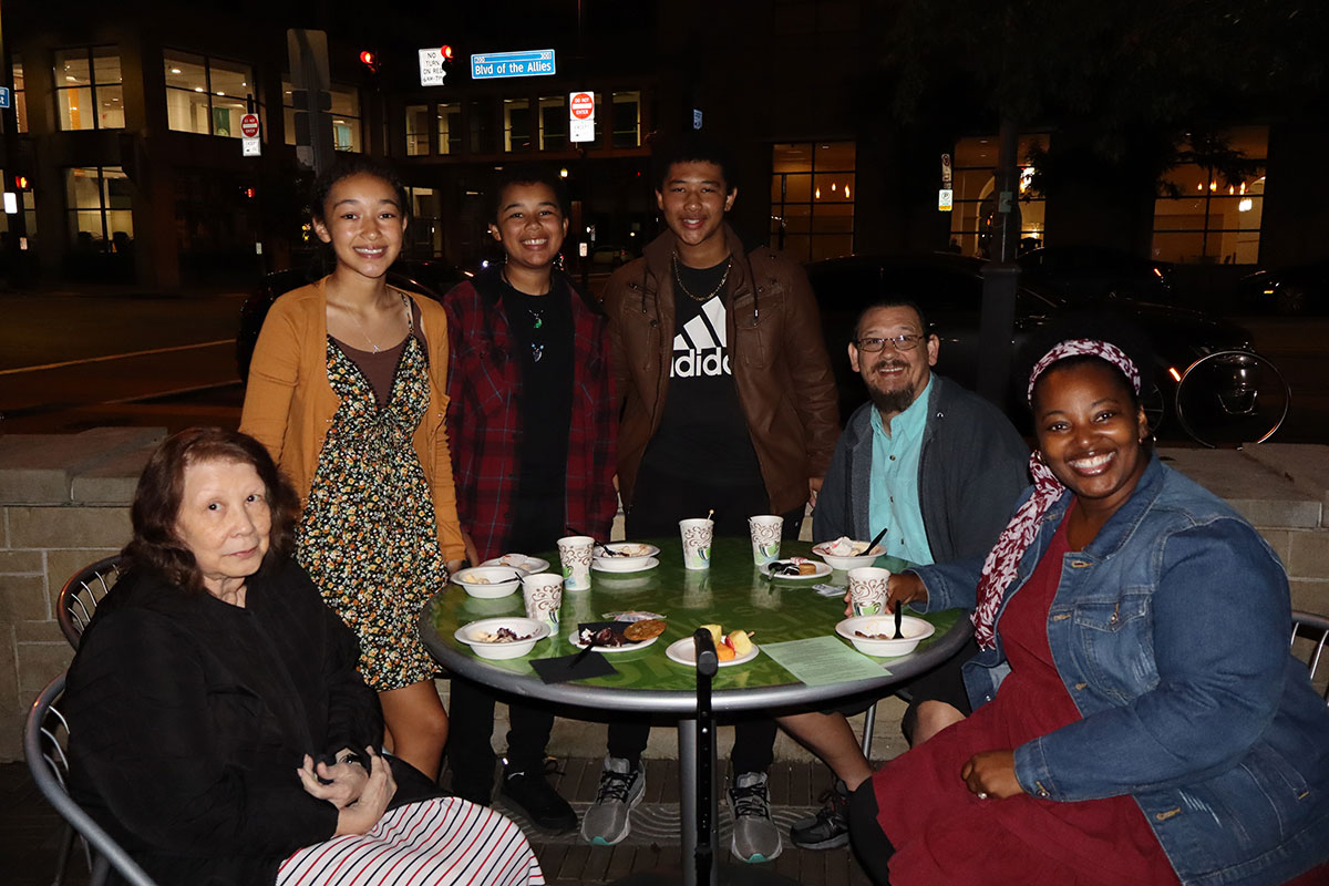 A family sits around a table in village park. 