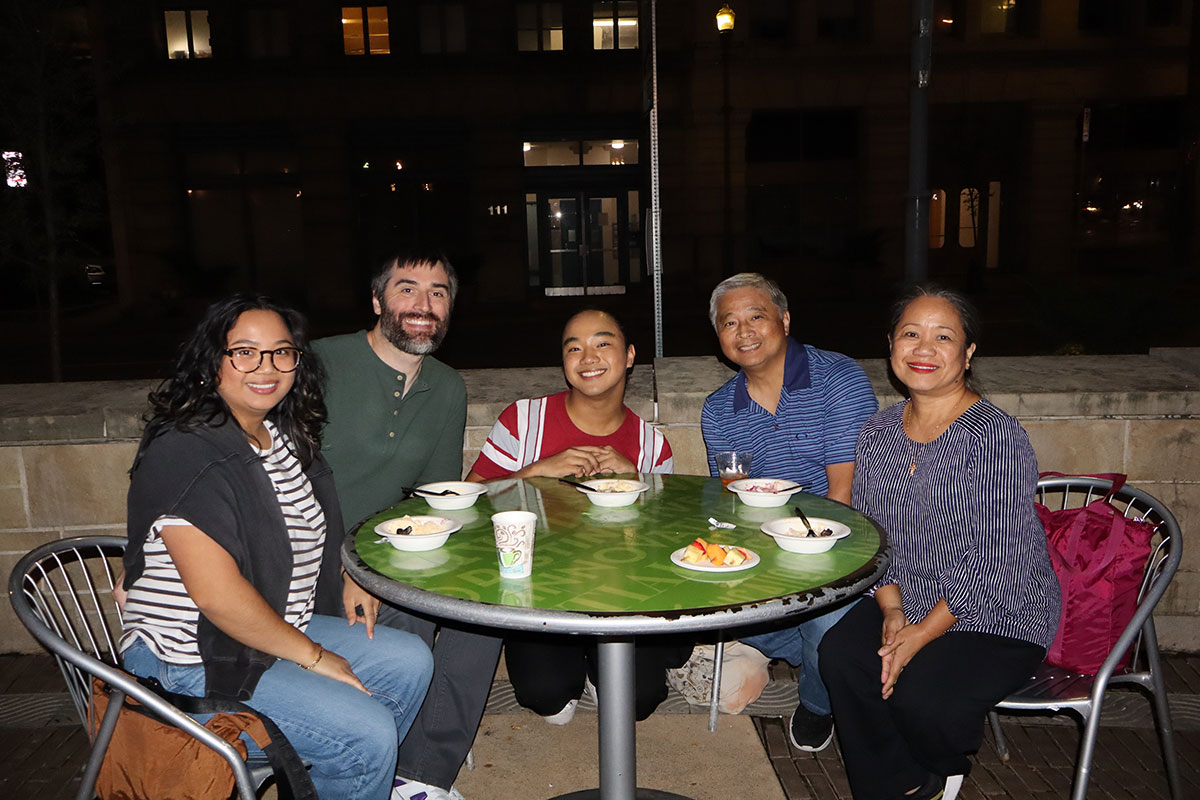 A family sits around a table in village park. 