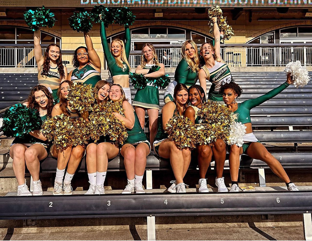 Cheer team poses on stadium bleachers.