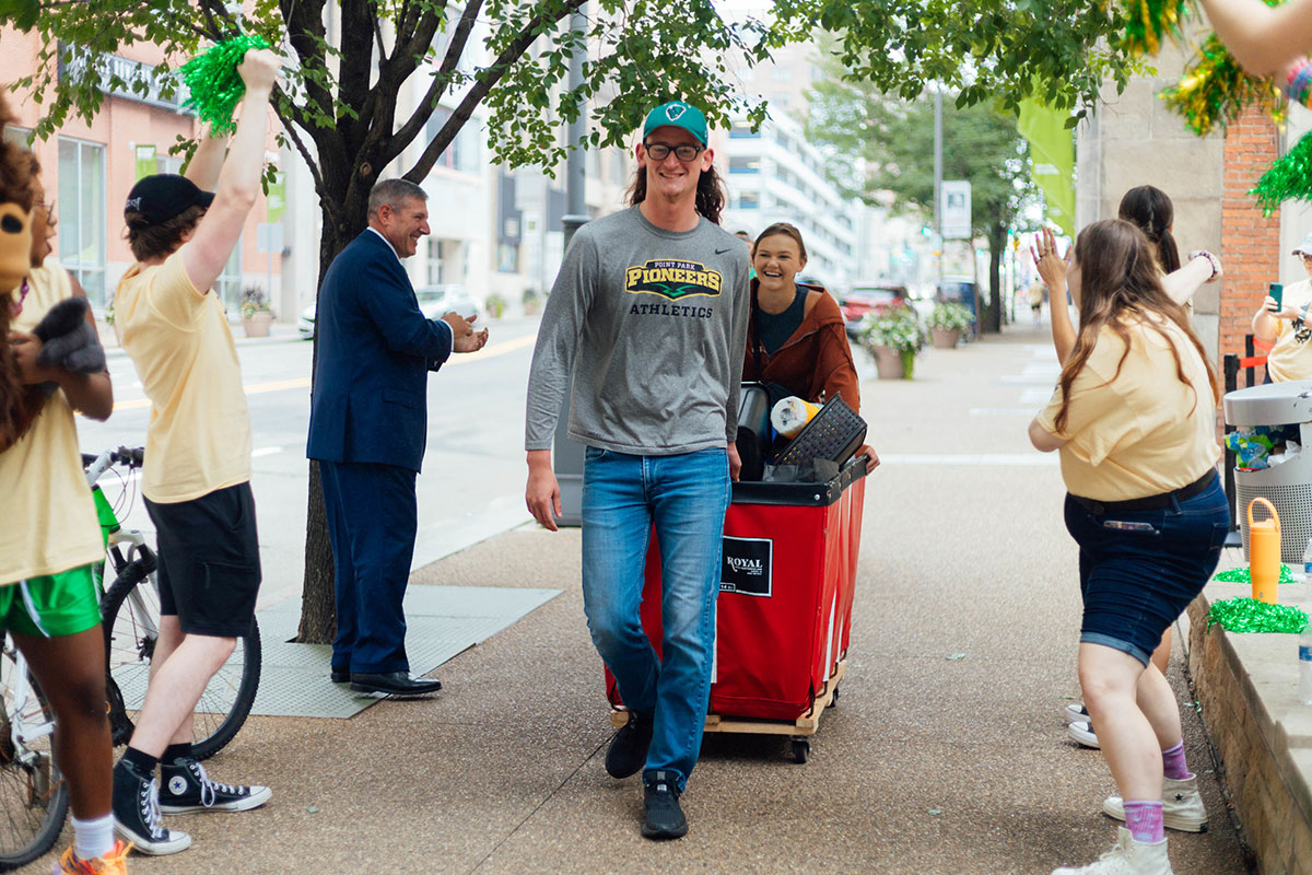 New Students walk with red bins full of items.