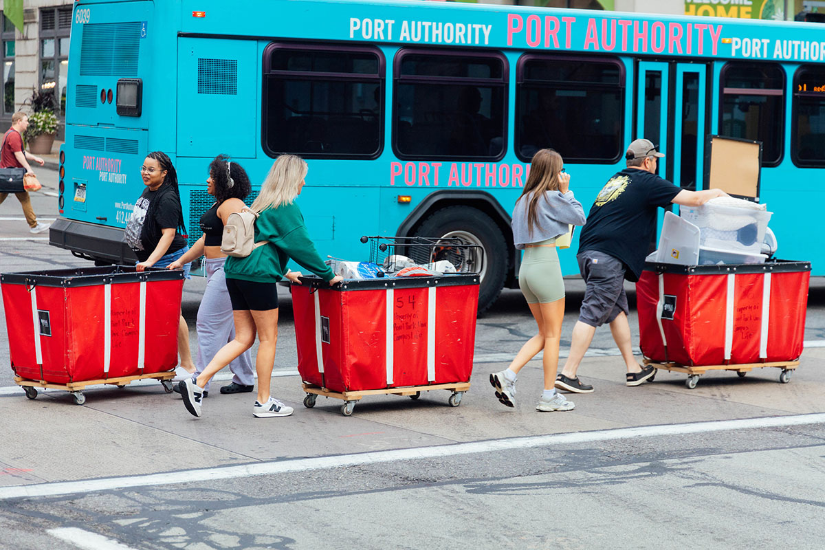 New Students walk with red bins full of items.